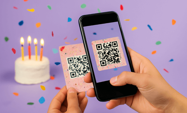 A close-up of a person scanning a festive QR code on a decorated card using a smartphone, with a birthday cake and confetti in the background.
